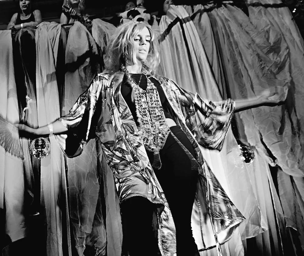 Model with open arms in front of hanging gowns, black and white